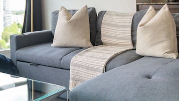Ett modernt vardagsrum med en grå soffa, ett soffbord i glas, en golvlampa och ett inramat, abstrakt konstverk på väggen.