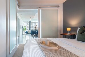 A modern hotel room with a large bed, a bedside table with a lamp, and a view of the cityscape through the window.