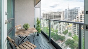 Ein Balkon mit Holztisch und -stühlen, einem Blumentopf und Blick auf hohe Gebäude.