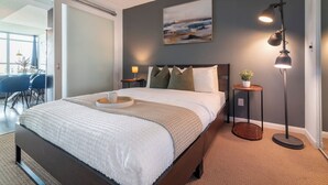 Ein modernes Schlafzimmer mit einem großen Bett, Nachttischlampen, einem kleinen Tisch mit Pflanze und einem Bild an der Wand.