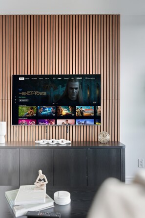 A flat-screen TV mounted on a wall with a wooden panel design, displaying a streaming service interface with various movie options. - Executive Toronto Condo Balcony & City Views (Toronto)