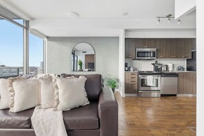 A modern living room with a brown leather sofa, a large window, and a view of the city. - Executive Toronto Condo Balcony & City Views (Toronto)