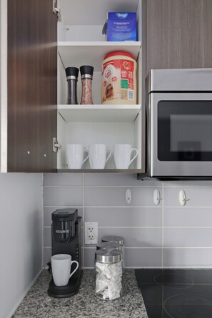 A kitchenette with a coffee maker, salt and pepper shakers, a coffee mug, a container of coffee creamer, and a microwave. - Executive Toronto Condo Balcony & City Views (Toronto)