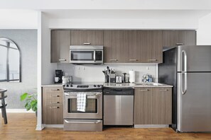 A modern kitchen with stainless steel appliances, wooden cabinets, and a view of the city through a window. - Executive Toronto Condo Balcony & City Views (Toronto)