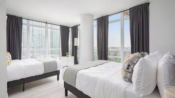 Ett hotellrum med två sängar, stora fönster och utsikt över staden.