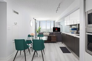 A modern kitchen with a built-in oven and a dining area with a glass table and green chairs. - Stylish 2BR Downtown Skyline Views & Free Parking | Parking Available (Toronto)