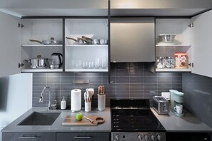 A modern kitchen with a built-in stove, a sink, and upper cabinets containing cookware and glassware. - Sunlit Studio w Balcony Views Prime Location! | Parking Available (Toronto)