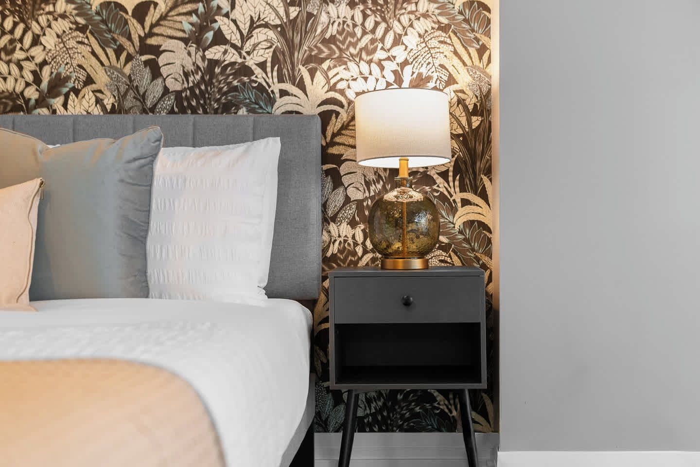 A bed with pillows, a nightstand with a lamp, and a wall with a floral pattern.