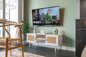 A living room with a television mounted on the wall, a white cabinet with wicker baskets, a wooden chair, and a potted plant. - Sunlit Studio w Balcony Views Prime Location! | Parking Available (Toronto)