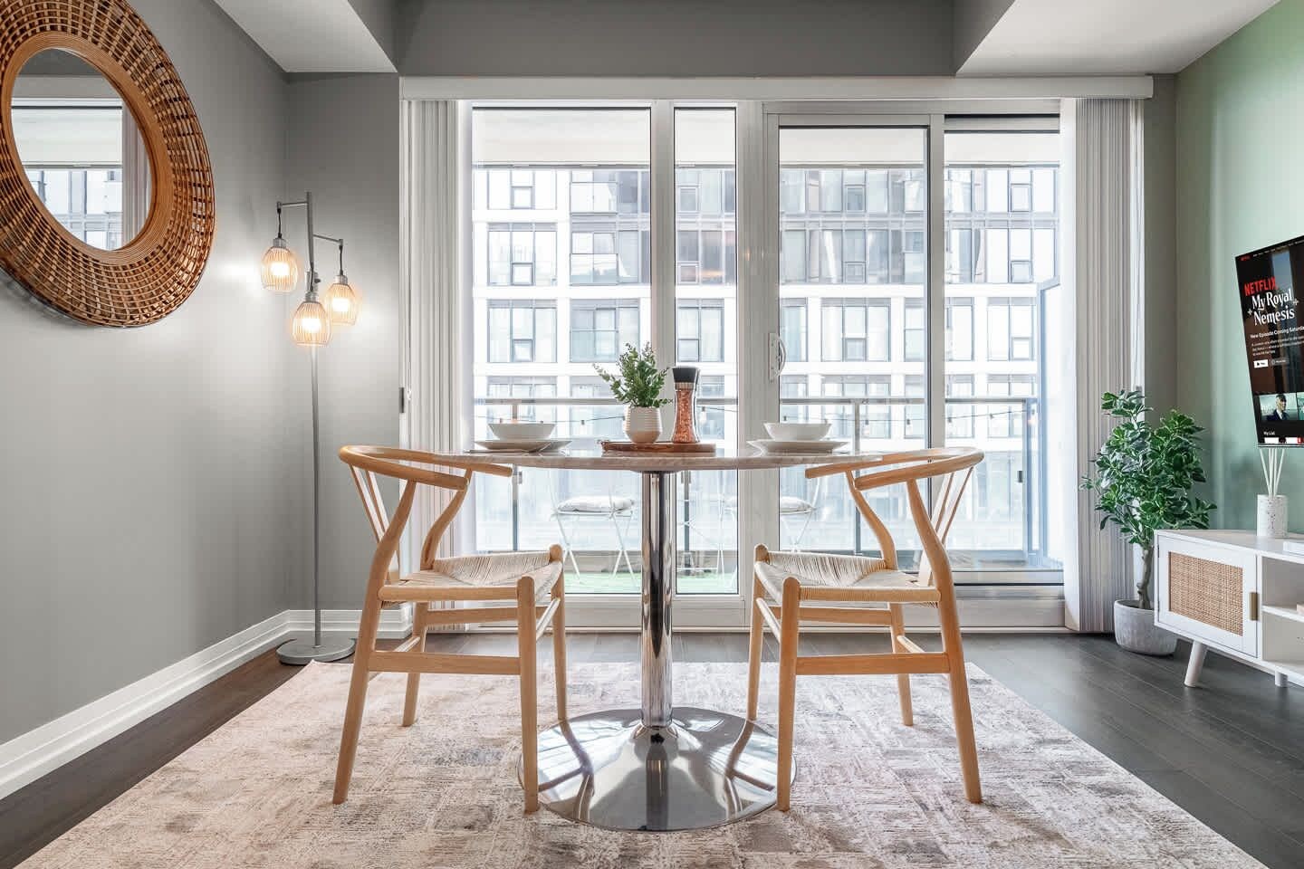 Un coin repas comprenant une table ronde, deux chaises, un miroir et un téléviseur posé sur un meuble.