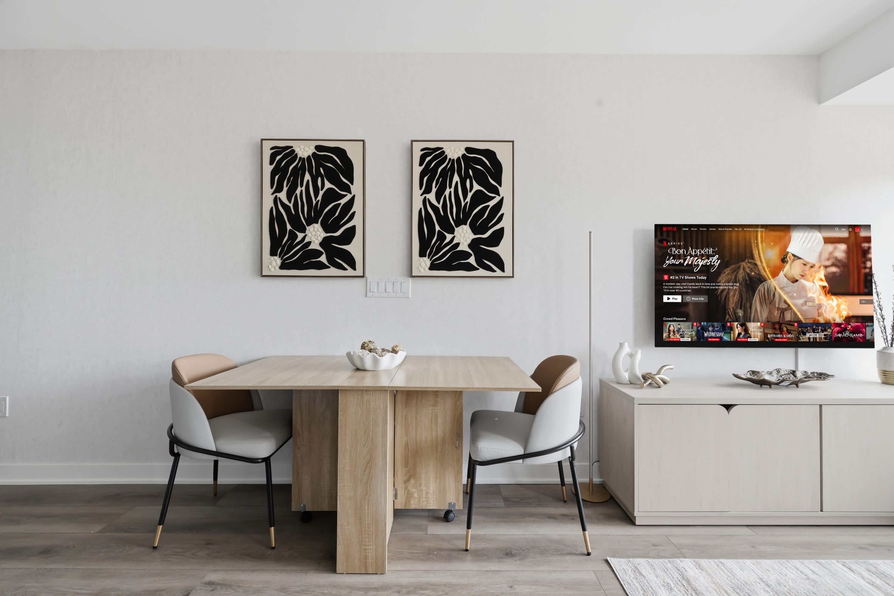 Un comedor moderno con una mesa de madera, cuatro sillas y dos obras de arte abstracto colgadas en la pared.