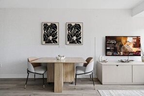 Een moderne eetruimte met een houten tafel, vier stoelen en twee abstracte kunstwerken aan de muur.