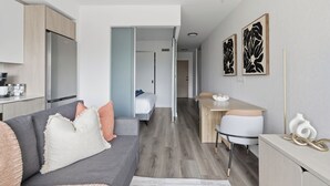 Um apartamento moderno com cozinha compacta, área de refeições, sala de estar com sofá e almofadas, e quarto com cama.