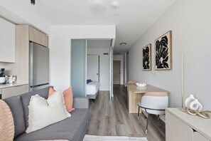 Een modern appartement met kitchenette, eethoek, woonkamer met bank en kussens, en slaapkamer met bed.