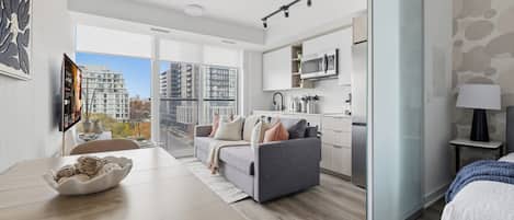 Un apartament modern amb zona de menjador, sofà, cuina i una finestra gran que ofereix vistes a la ciutat.