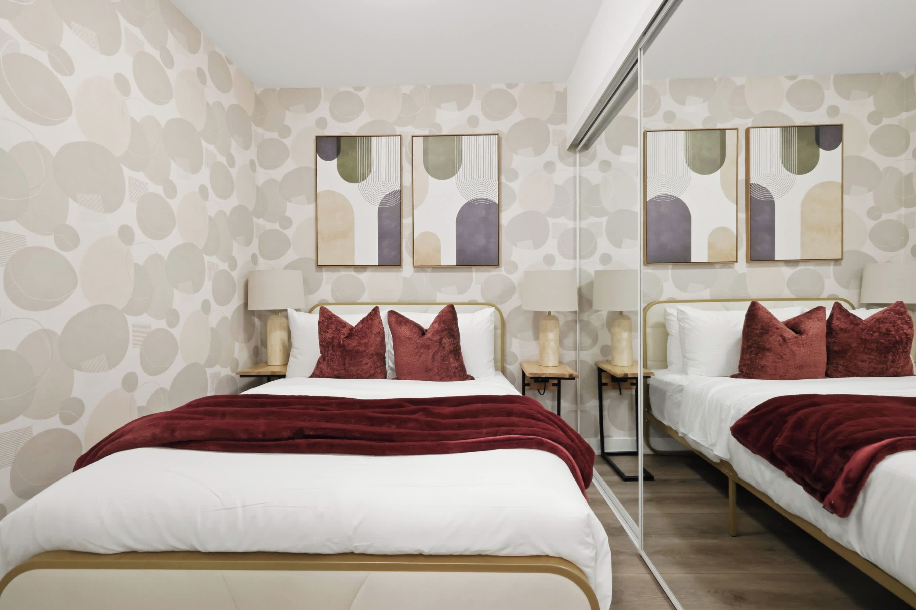A hotel room with a mirrored wall, two beds with red bedding, and artwork above the beds.