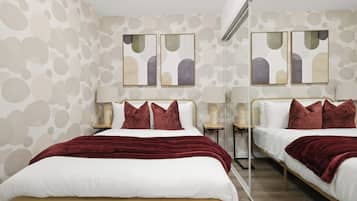 Habitación de hotel con una pared espejada, dos camas con ropa de cama roja y obras de arte sobre ellas.