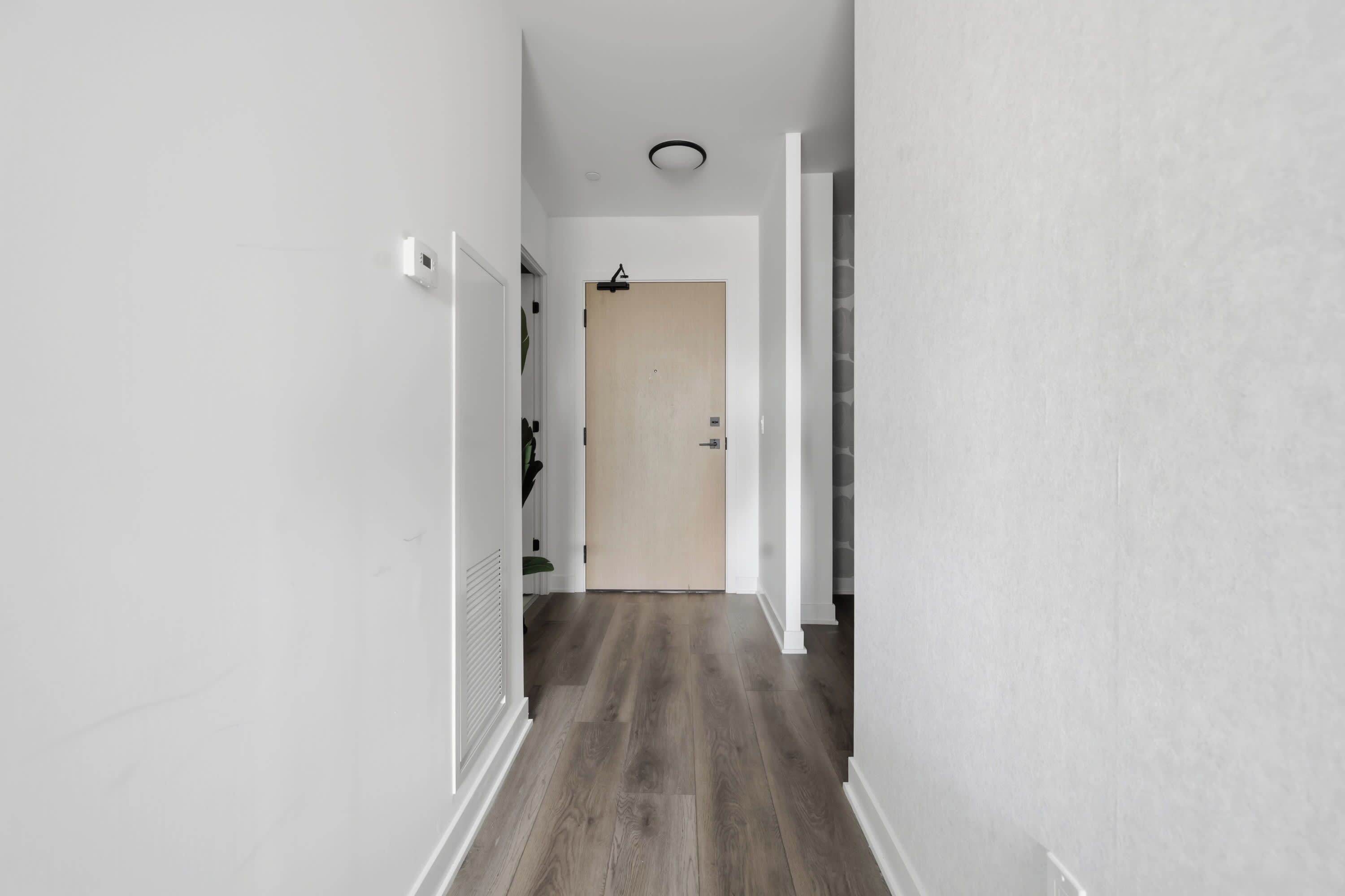 Un pasillo estrecho con suelo de madera, paredes blancas y una puerta al final.