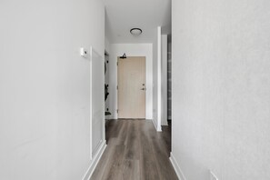 A narrow hallway with a wooden floor, white walls, and a door at the end.