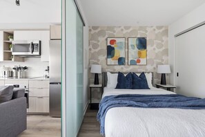 Een moderne hotelkamer met een bed, nachtkastjes, een keukenhoek en abstracte wanddecoratie.