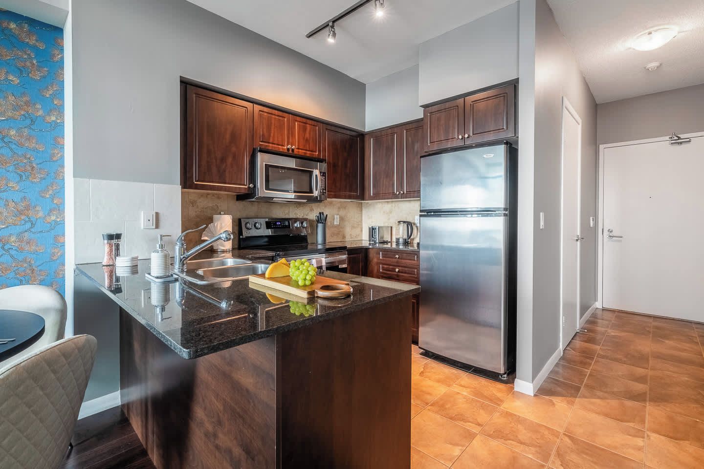 A modern kitchen with dark wooden cabinets, stainless steel appliances, and a granite countertop.