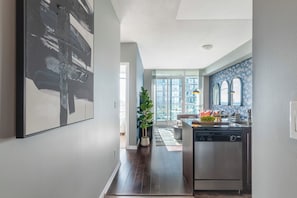A modern kitchen with a dishwasher, a dining area with a table and chairs, and a large window providing a view of the cityscape.