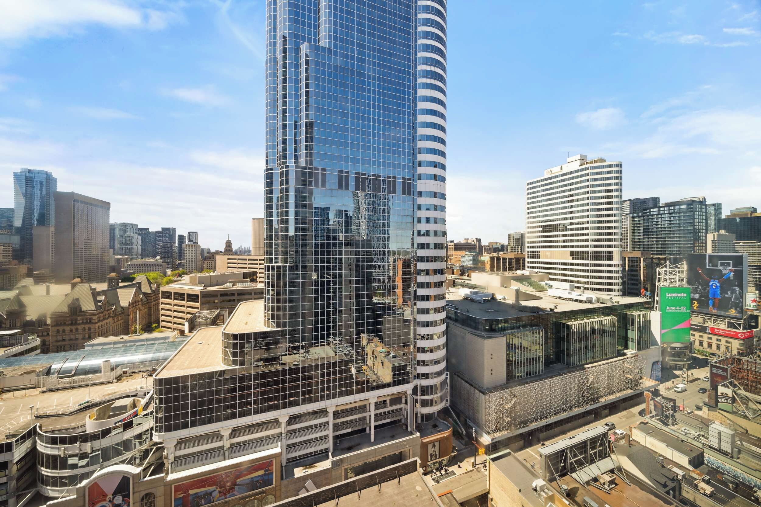 Een modern hoog gebouw met een glazen gevel, omringd door andere stadsgebouwen.