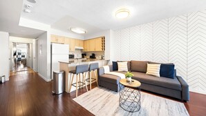 A modern living room with a sofa, coffee table, and bar stools. - Modern Downtown Studio Steps to Yonge-Dundas (Toronto)