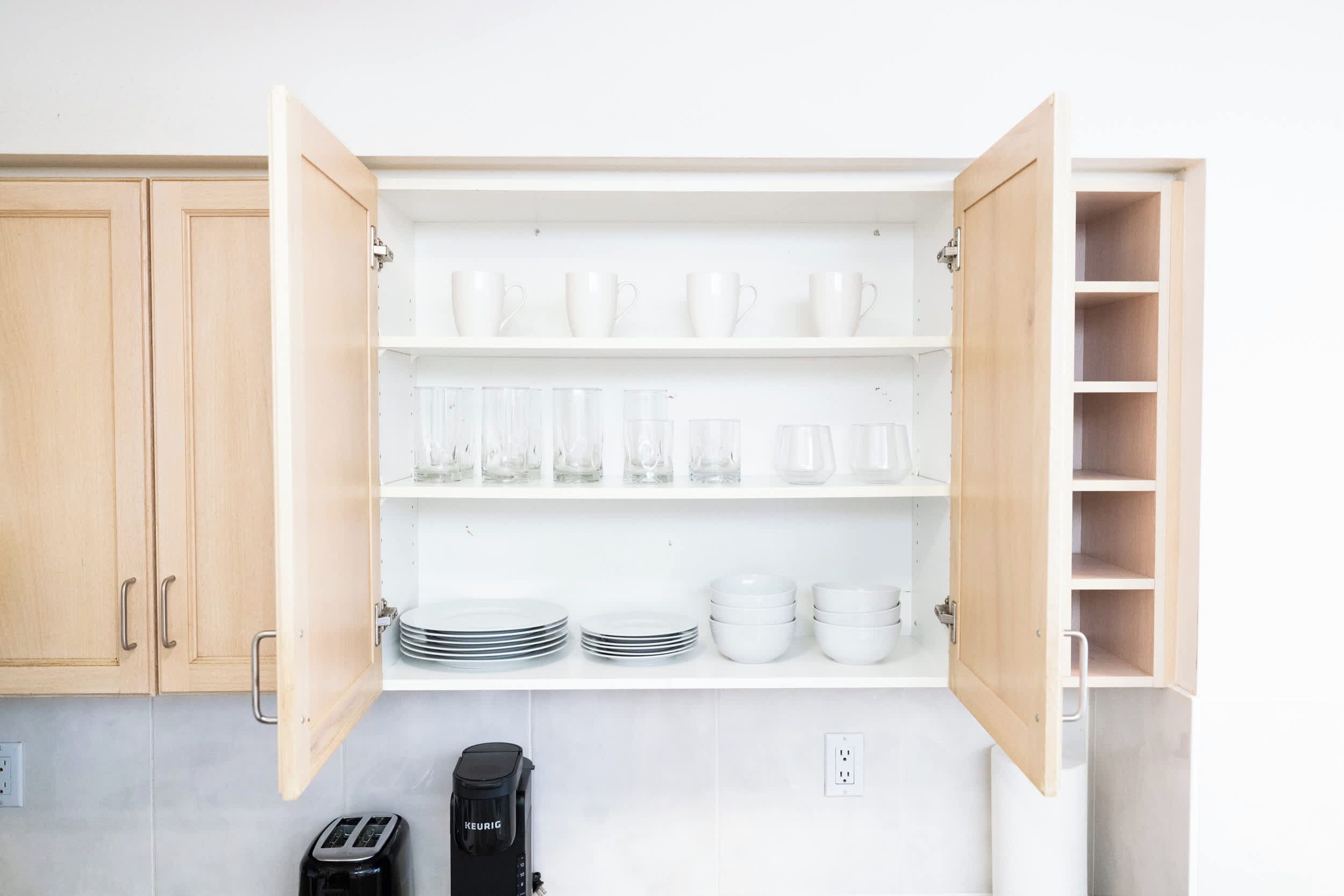 Cocina con alacenas abiertas que exhiben vajilla blanca, vasos y una cafetera.