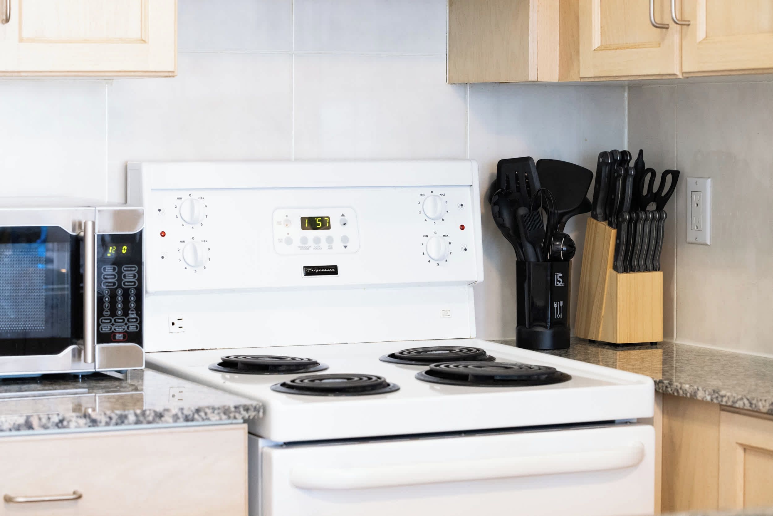 Una cocina con estufa blanca, microondas y un bloque de cuchillos.