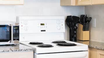 Una cocina con estufa blanca, microondas y un bloque de cuchillos.