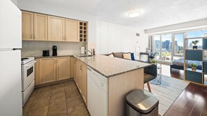 A modern kitchen with a central island, wooden cabinets, and a view of the city through large windows. - Modern Downtown Studio Steps to Yonge-Dundas (Toronto)