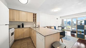Een moderne keuken met een centraal eiland, houten kastjes en uitzicht op de stad door grote ramen.