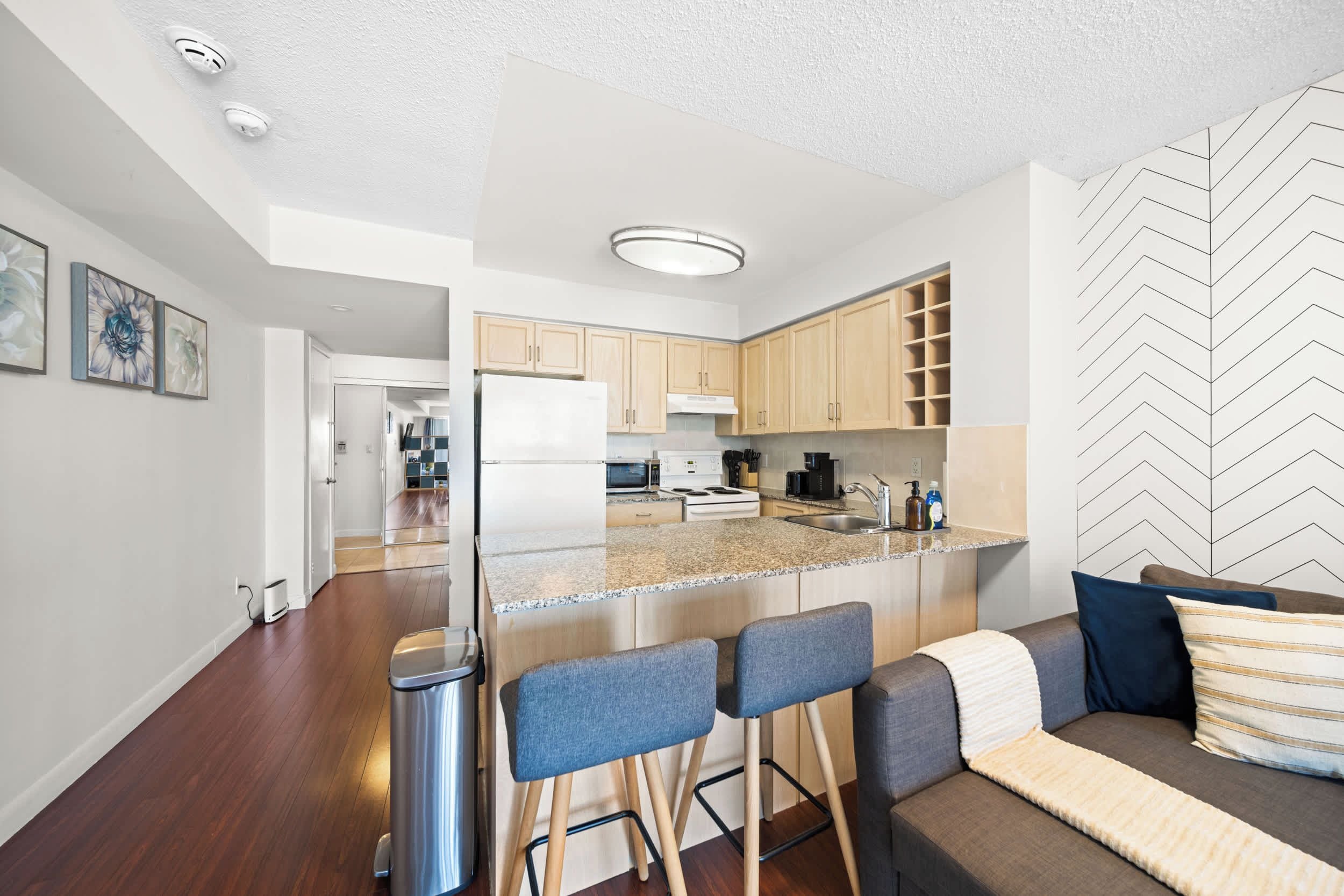 Una cocina moderna con una isla central, taburetes de bar y una zona de estar con sofá y cojines.