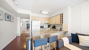 Una cocina moderna con una isla central, taburetes de bar y una zona de estar con sofá y cojines.