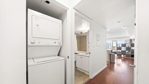 A laundry room with stacked washers and dryers, a kitchen with a sink and cabinets, and a view of the city through large windows. - Modern Downtown Studio Steps to Yonge-Dundas (Toronto)