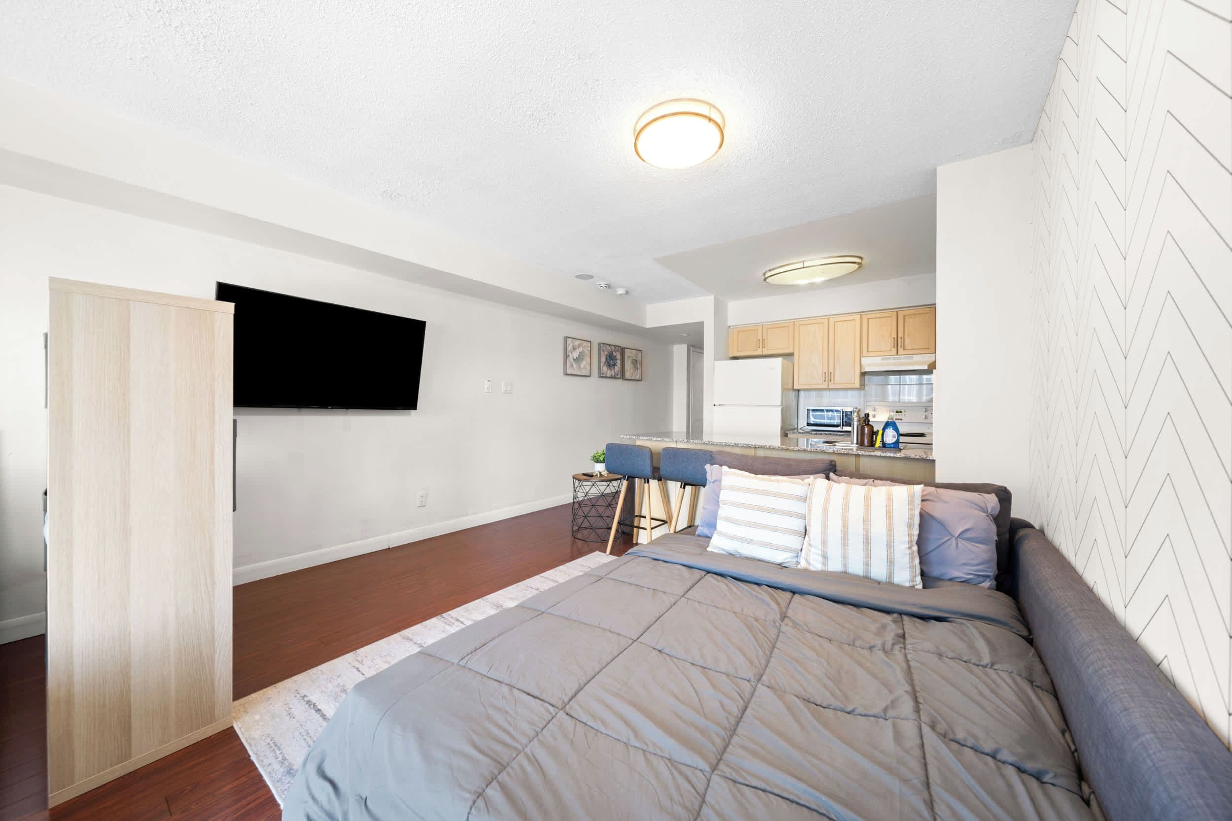Un apartamento moderno con una cama grande, un televisor montado en la pared, una zona de cocina y una mesa de comedor con sillas.