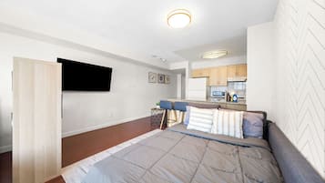 Un apartamento moderno con una cama grande, un televisor montado en la pared, una zona de cocina y una mesa de comedor con sillas.