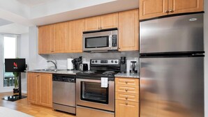 A modern kitchen with wooden cabinets, a stainless steel refrigerator, a microwave, an oven, a dishwasher, and a coffee maker. - Bright Waterfront Studio Steps to DT Toronto (Toronto)