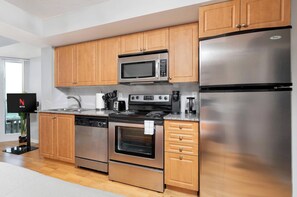 Eine moderne Küche mit Holzschränken, einem Edelstahlkühlschrank, einer Mikrowelle, einem Backofen, einem Geschirrspüler und einer Kaffeemaschine.