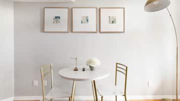 A minimalist dining area with a round table, two chairs, a vase with flowers, and a floor lamp.