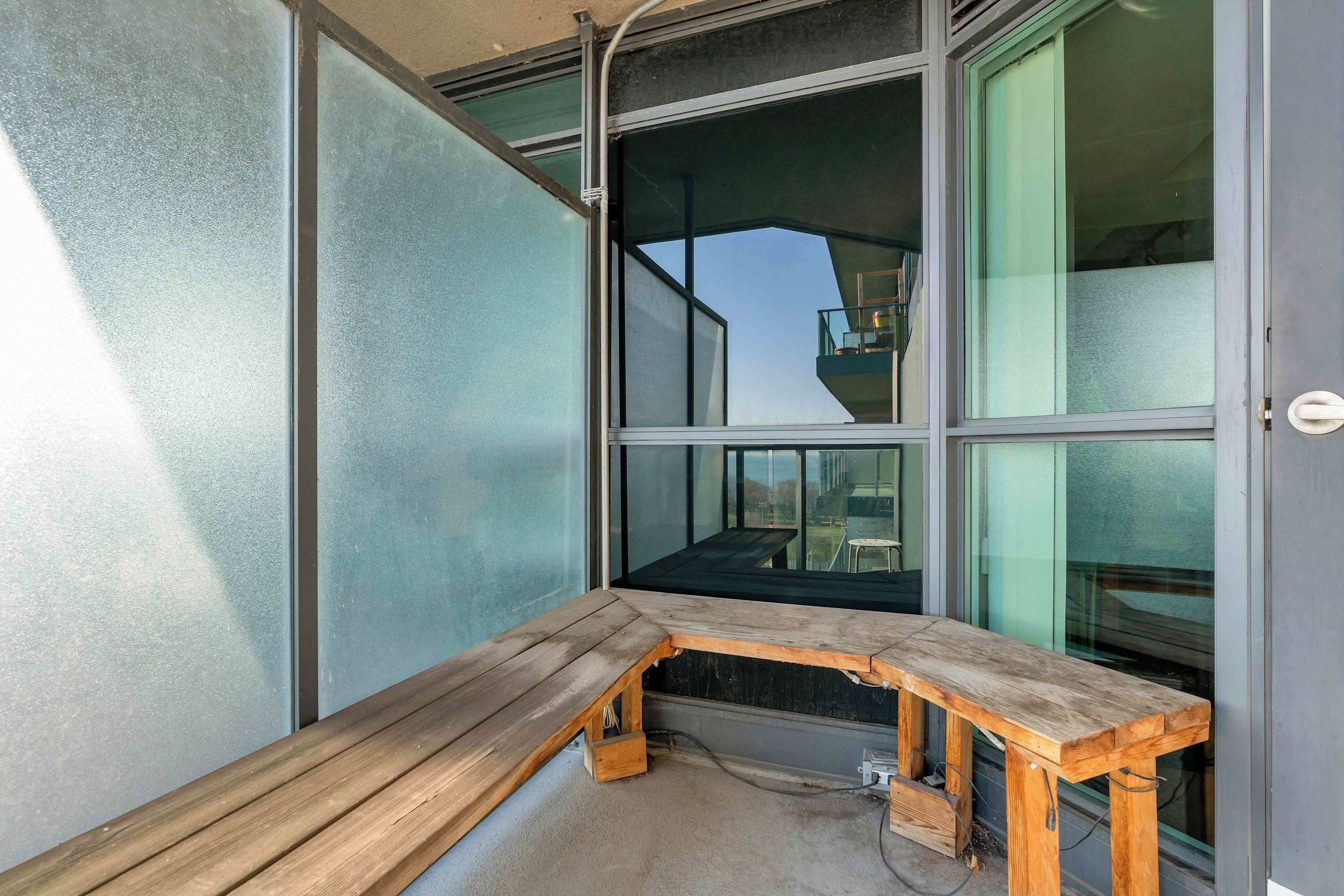 A corner of a room with a wooden bench, large windows, and a view of the outside.