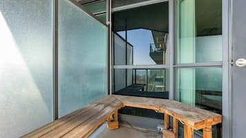 A corner of a room with a wooden bench, large windows, and a view of the outside.