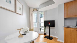 A modern kitchen with a dining area, a flat-screen TV mounted on the wall, and a view of the outside through a window. - Bright Waterfront Studio Steps to DT Toronto (Toronto)