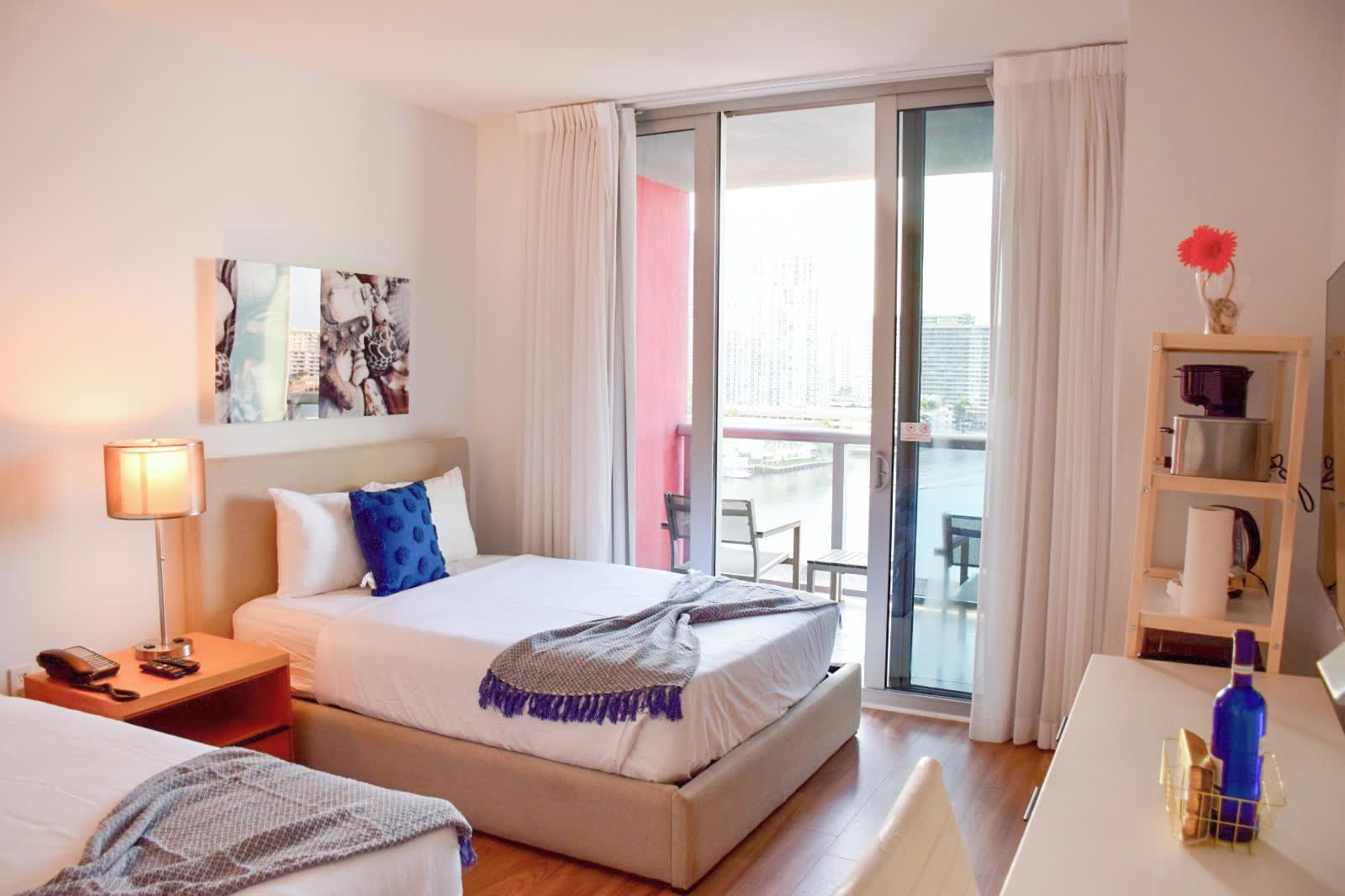 Une chambre d’hôtel avec un lit, un bureau, une chaise, une lampe, un tableau et une vue sur l’extérieur.