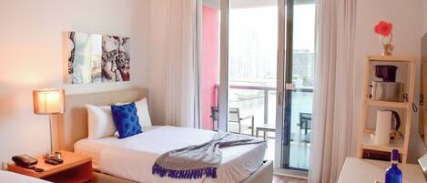 Une chambre d’hôtel avec un lit, un bureau, une chaise, une lampe, un tableau et une vue sur l’extérieur.
