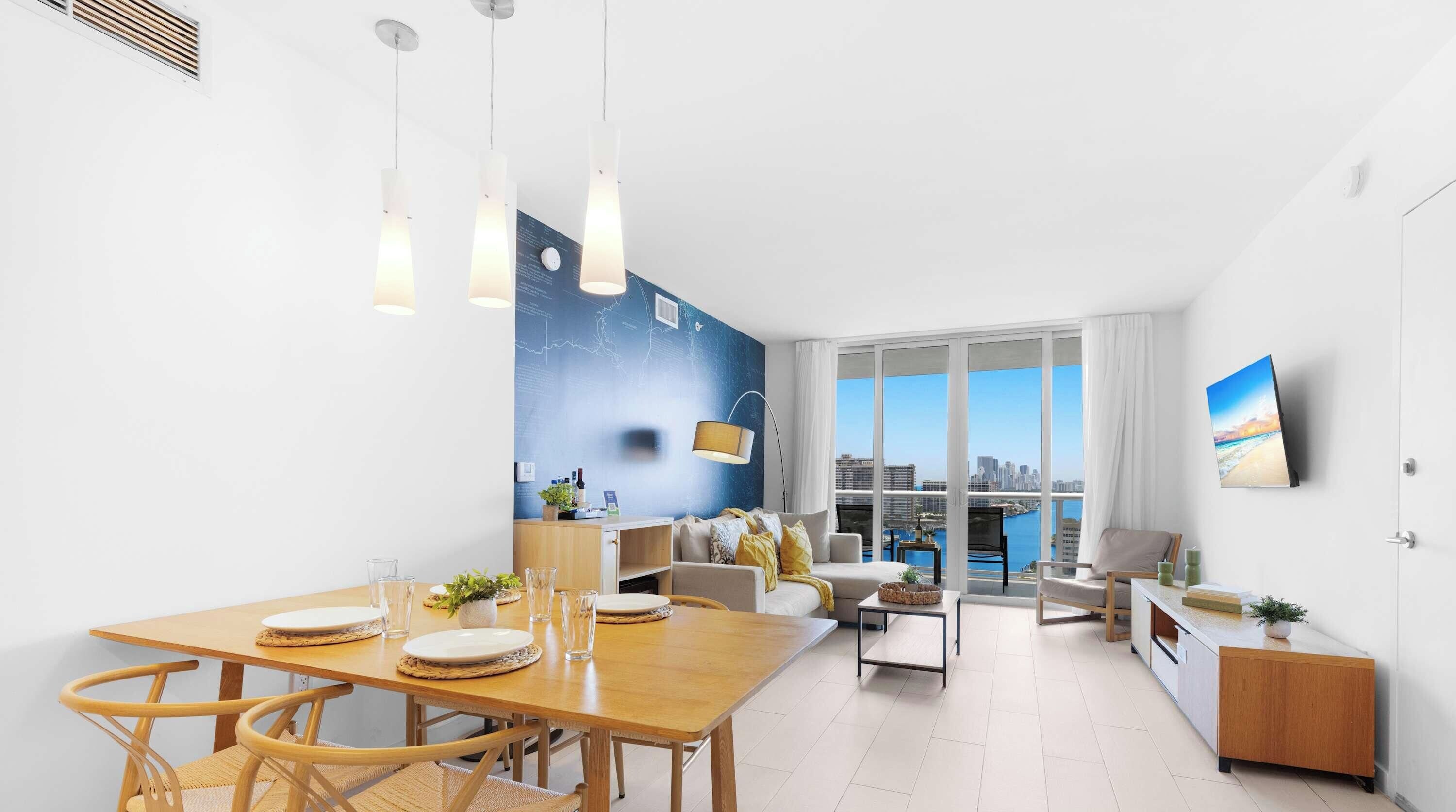 A modern living room with a city view, a dining area with a wooden table, and a large window.