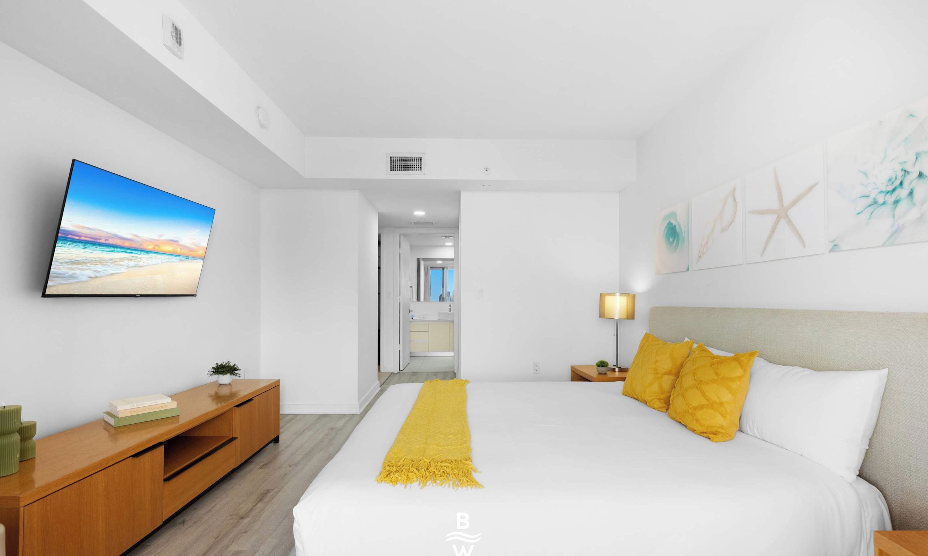 Una habitación de hotel con cama, televisión, mesita de noche, lámpara y una obra de arte en la pared.