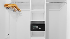 Une armoire blanche avec un coffre-fort noir et des cintres en bois.