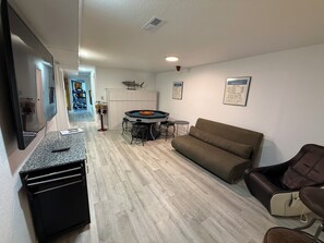 A living room with a sofa, a gaming table, and a TV.